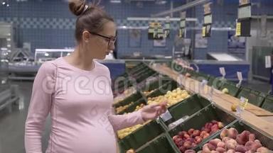 在<strong>超市</strong>里戴眼镜的年轻孕妇选择新鲜的有机<strong>水果</strong>。 女人在购物时选择<strong>水果</strong>。
